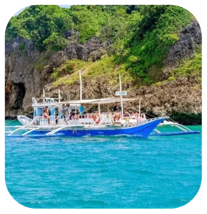 Traditional Filipino outrigger boat carrying tourists along a rocky island coastline in clear blue waters
