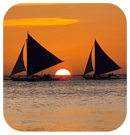 Traditional paraw sailboats silhouetted against a Boracay sunset over calm waters