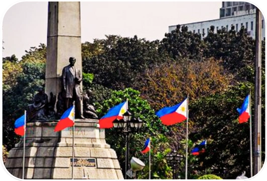 Rizal Monument in Luneta Park Manila with surrounding Philippine flags under bright daylight